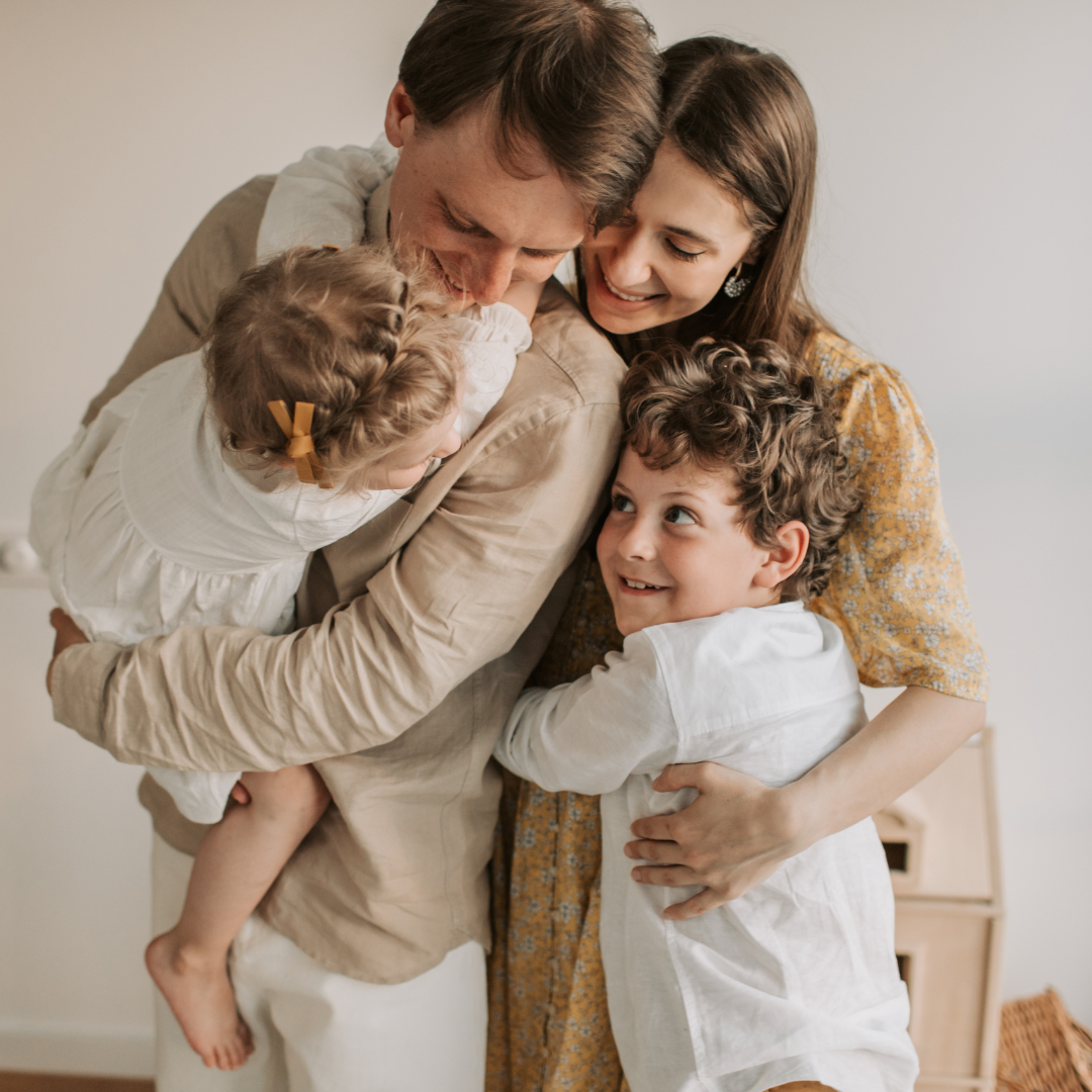 A mother, father and two young children embracing at home